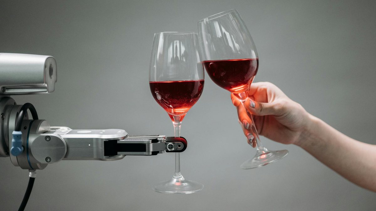 Ein Roboterarm und eine menschliche Hand stoßen mit zwei Weingläsern an.