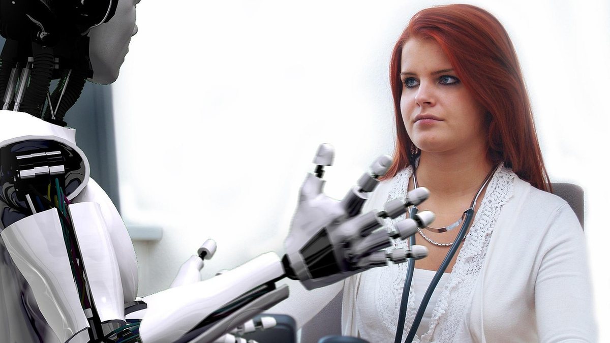 Ein humanoider Roboter sitzt einer jungen Frau am Schreibtisch gegenüber, wie in einem Beratungsgespräch.